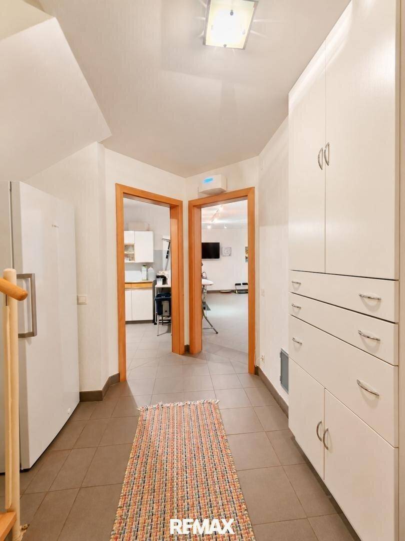 Heller Flur mit Einbauschränken, Kühlschrank und Zugang zu Küche und Wohnzimmer.