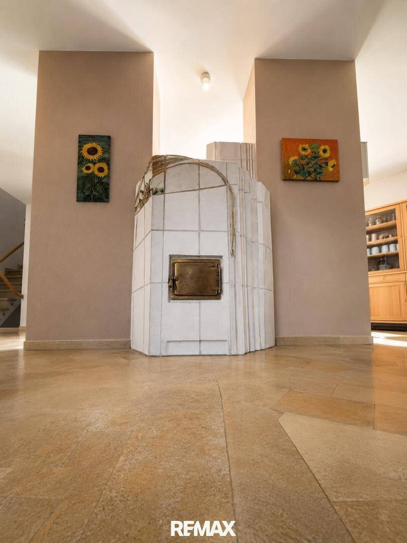 Traditioneller Kachelofen in einem hellen Wohnbereich mit Steinboden und Kunstwerken.