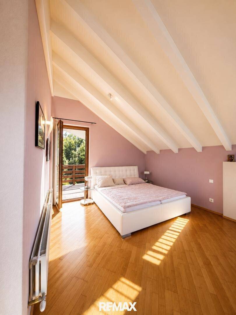 Helles Schlafzimmer mit Holzboden, Dachschräge und Zugang zu einem Balkon.