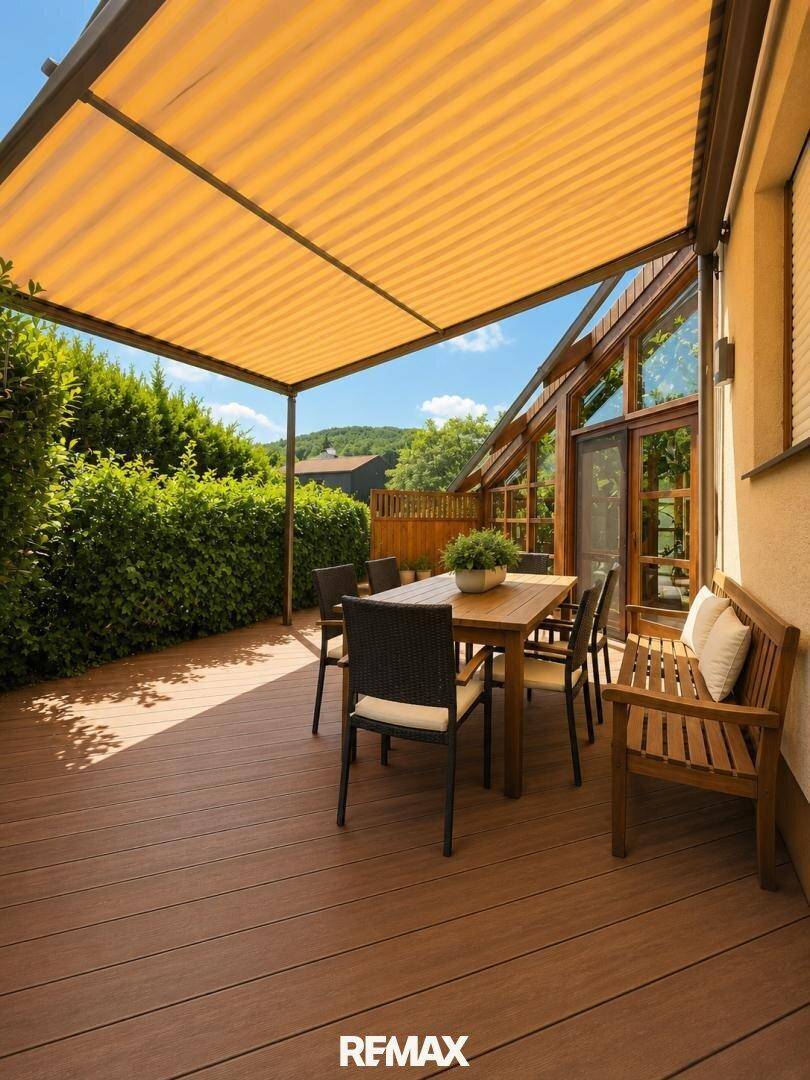 Überdachte Terrasse mit Holzboden, Esstisch und Blick ins Grüne.