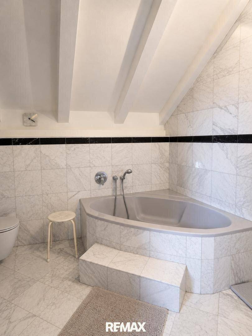 Badezimmer mit Marmorfliesen, Eckbadewanne und Dachschräge.