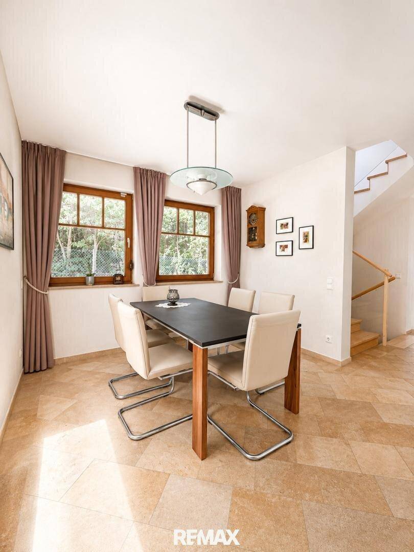 Heller Essbereich mit Holztisch, modernen Stühlen und Blick ins Grüne durch die Fenster.