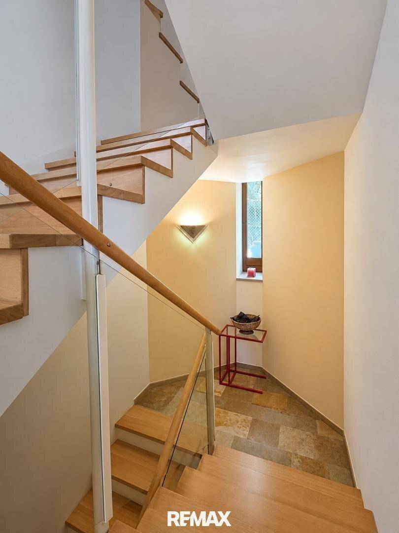 Helle Holztreppe mit Glasgeländer und Fenster, die die Ebenen verbindet.