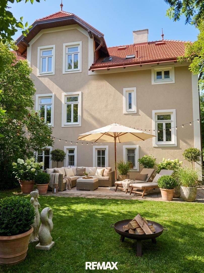 Großzügige Terrasse mit bequemen Gartenmöbeln, Sonnenschirm und Feuerstelle im grünen Gartenbereich.