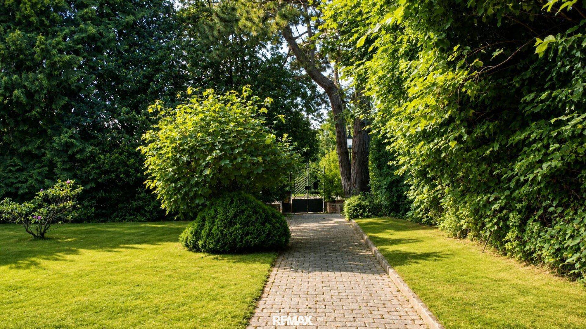 Grüner Garten mit gepflastertem Weg und hohen Bäumen, der zu einem schmiedeeisernen Tor führt.