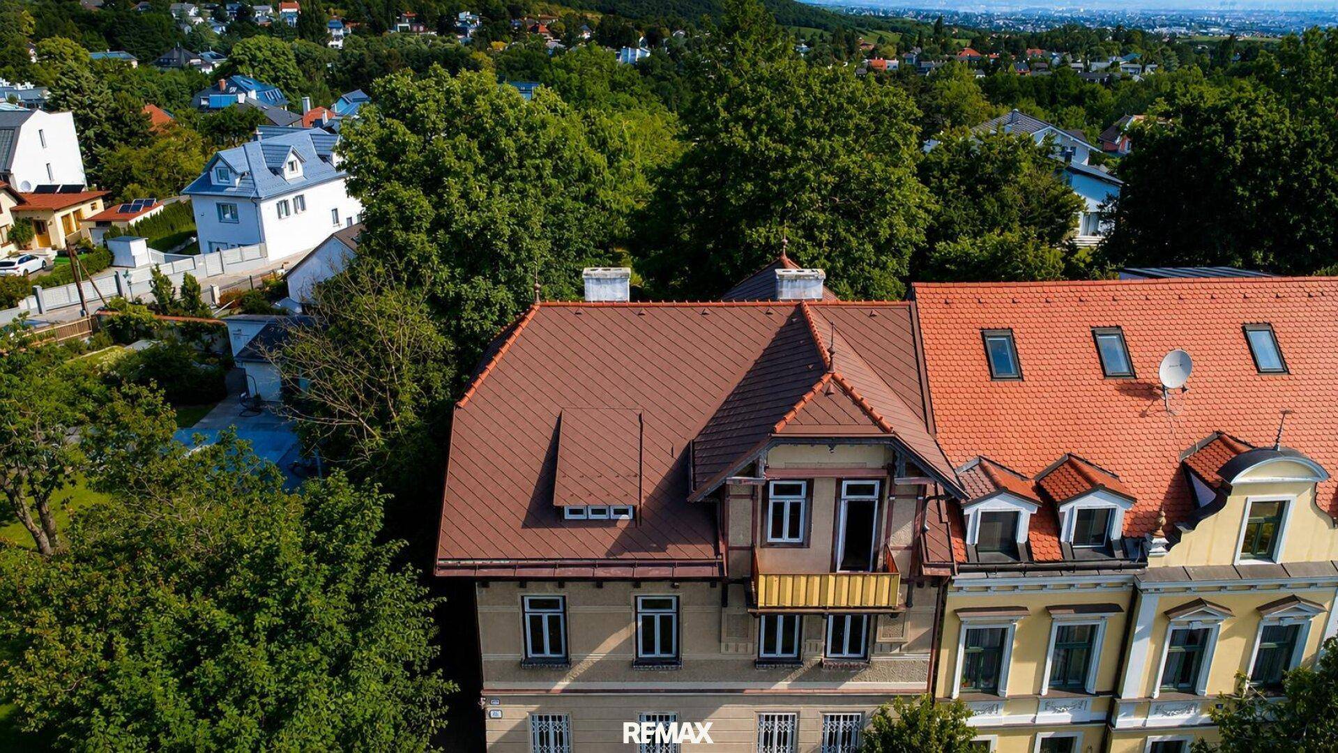 Luftaufnahme der Dächer der Villa und eines Nachbargebäudes, umgeben von dichtem Baumbestand.