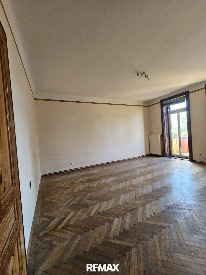 Geräumiges Zimmer mit Fischgrätparkett, hellen Wänden und Zugang zu einem Balkon oder einer Terrasse.