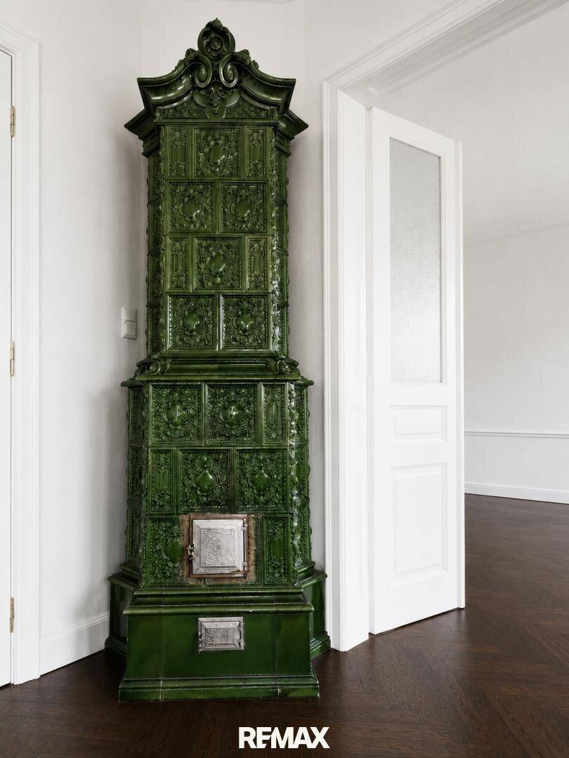 Detailaufnahme eines prächtigen, grünen Kachelofens mit kunstvollen Verzierungen in einem hellen Raum.
