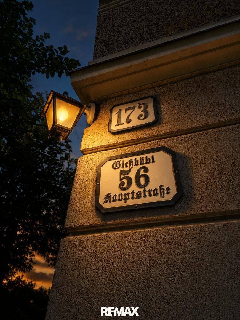 Hausnummern und Straßenname an einer historischen Fassade mit einer klassischen Laterne bei Dämmerung.
