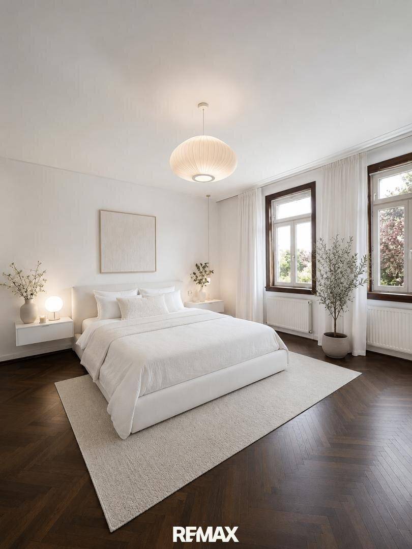 Ruhiges Schlafzimmer mit dunklem Fischgrätparkett, weißem Bett und großen Fenstern mit Vorhängen.