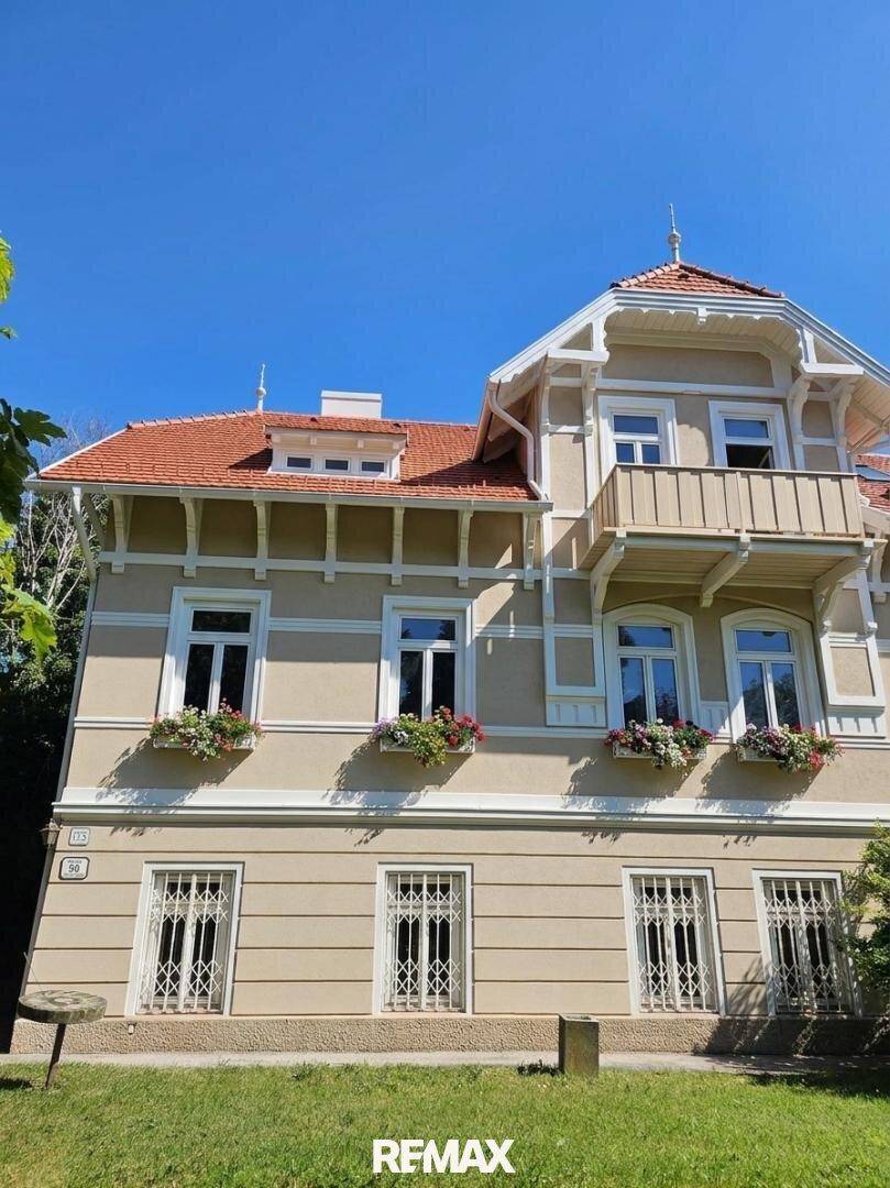 Historische Villa mit aufwendiger Fassadengestaltung, Balkon und Blumenkästen unter den Fenstern.