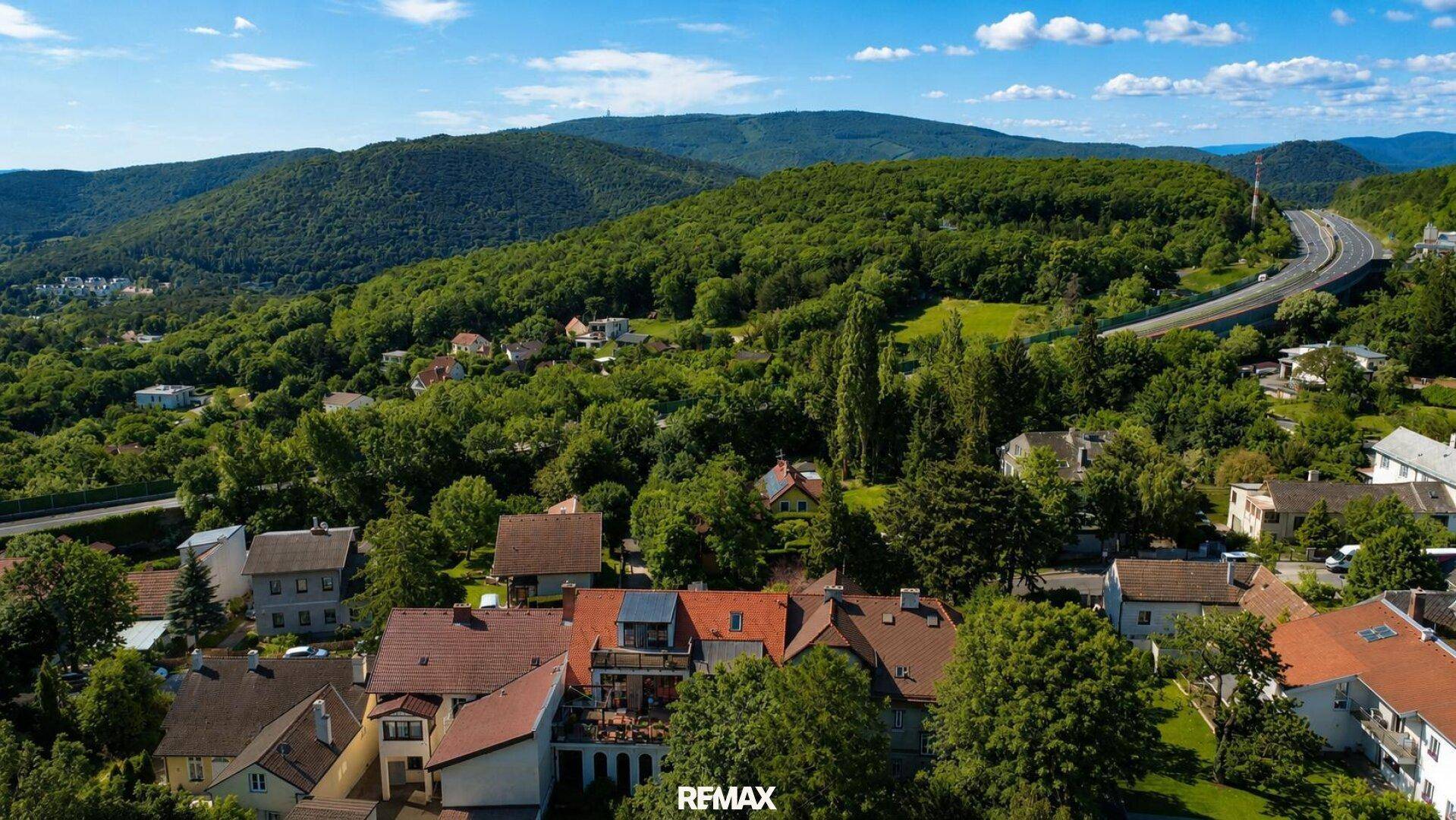Panoramablick auf eine Stadt in einem Tal mit bewaldeten Hügeln und einer Autobahn in der Ferne.