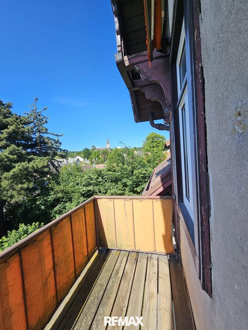 Kleiner, alter Balkon mit Holzboden und Blick über die Baumwipfel auf die Umgebung.