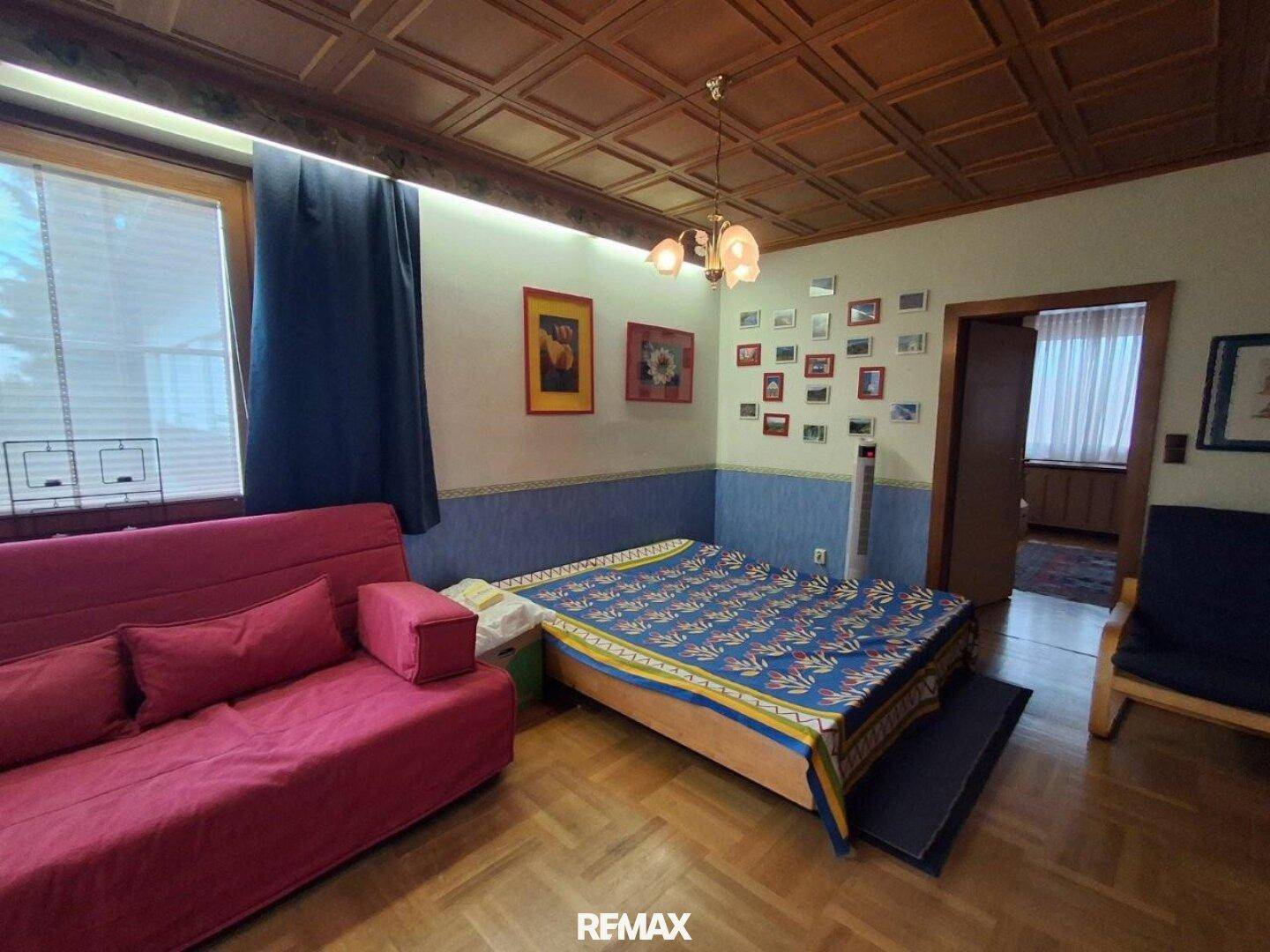 Schlafzimmer mit Holzkassettendecke, Parkettboden und farbenfroher Bettwäsche.