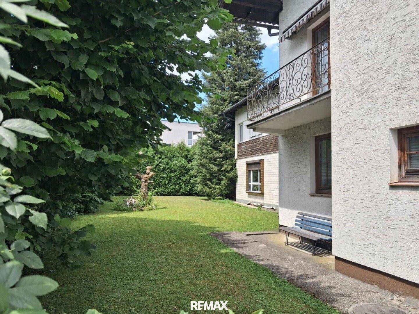 Gepflegter Gartenbereich mit Rasenfläche, Bäumen und einer Sitzbank am Haus.