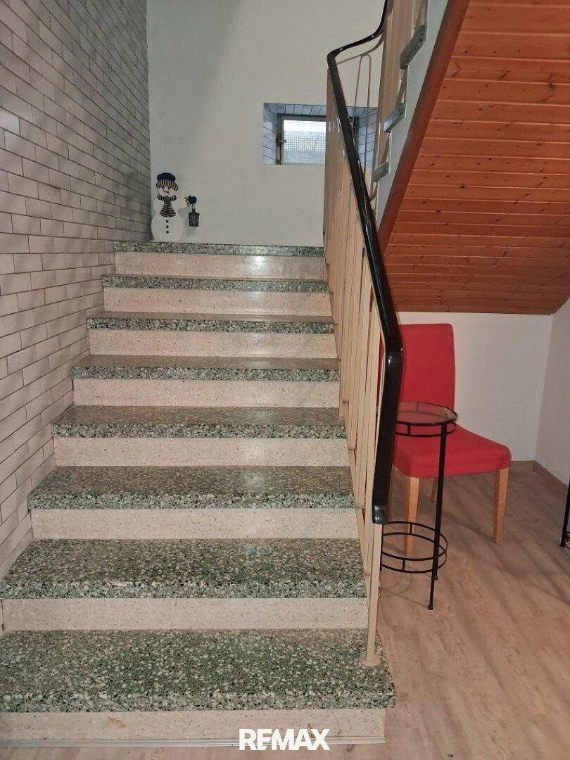 Treppenhaus mit Terrazzostufen, Holzgeländer und einer Ziegelwandverkleidung.