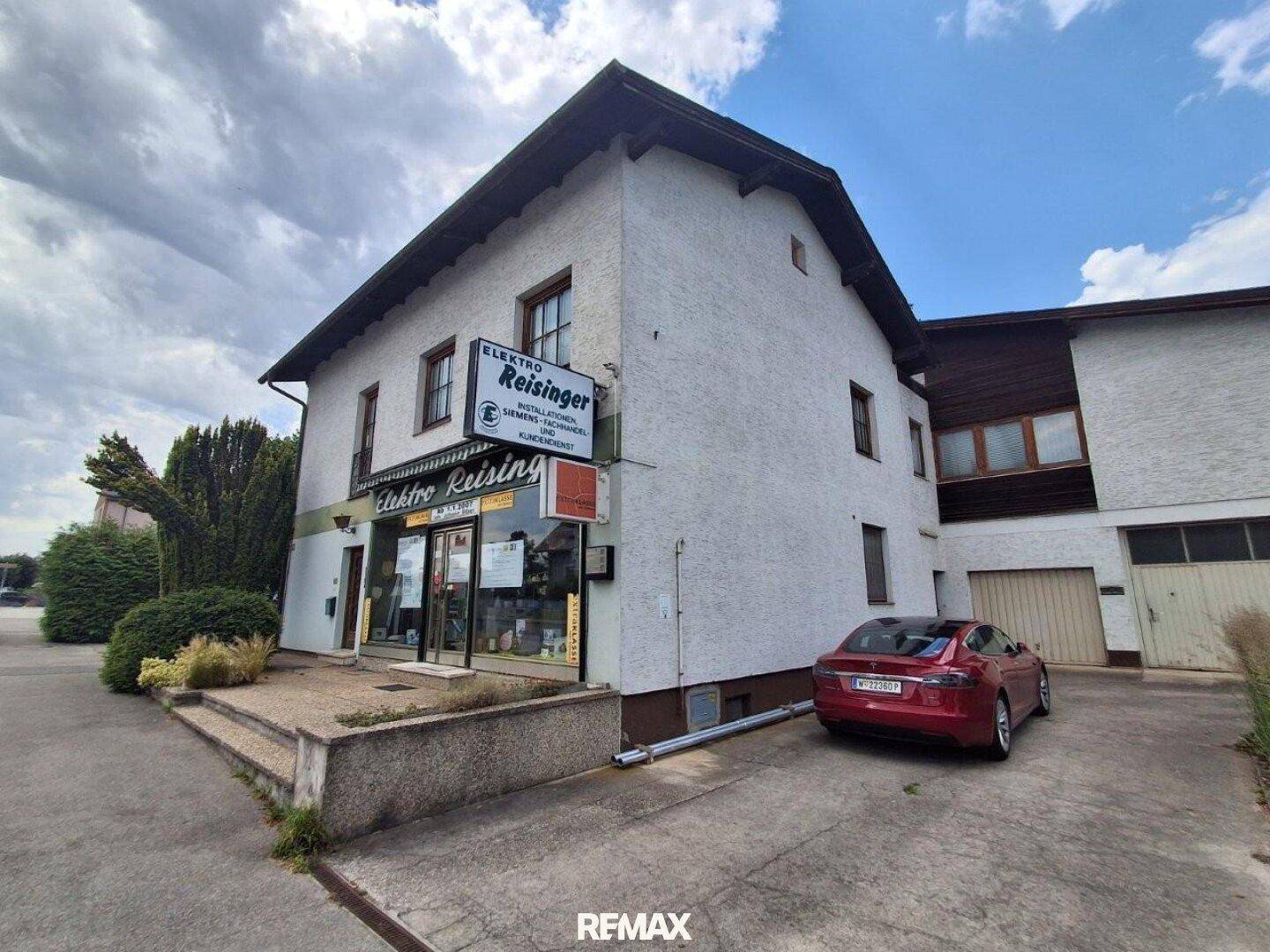 Mehrfamilienhaus mit Geschäftsfläche im Erdgeschoss und Parkplatz für Fahrzeuge.