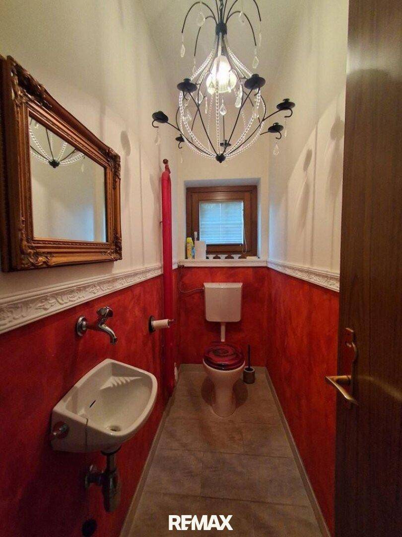 Gäste-WC mit roter Wandgestaltung, kleinem Waschbecken und Fenster.