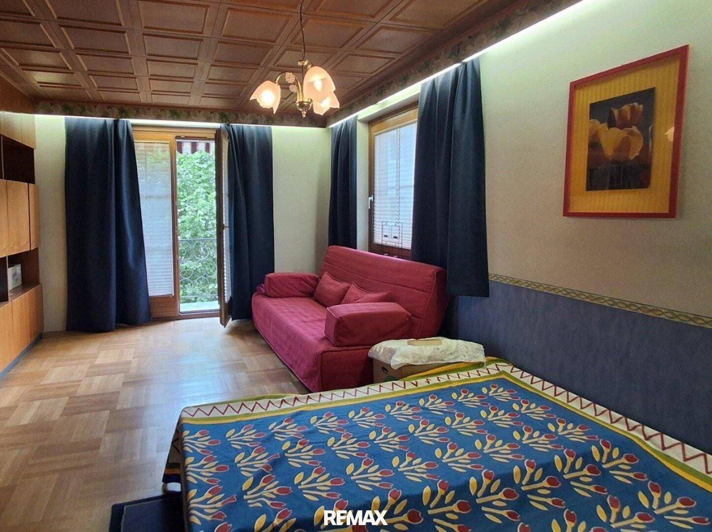 Gemütliches Schlafzimmer mit Holzkassettendecke, Parkettboden und Zugang zum Balkon.