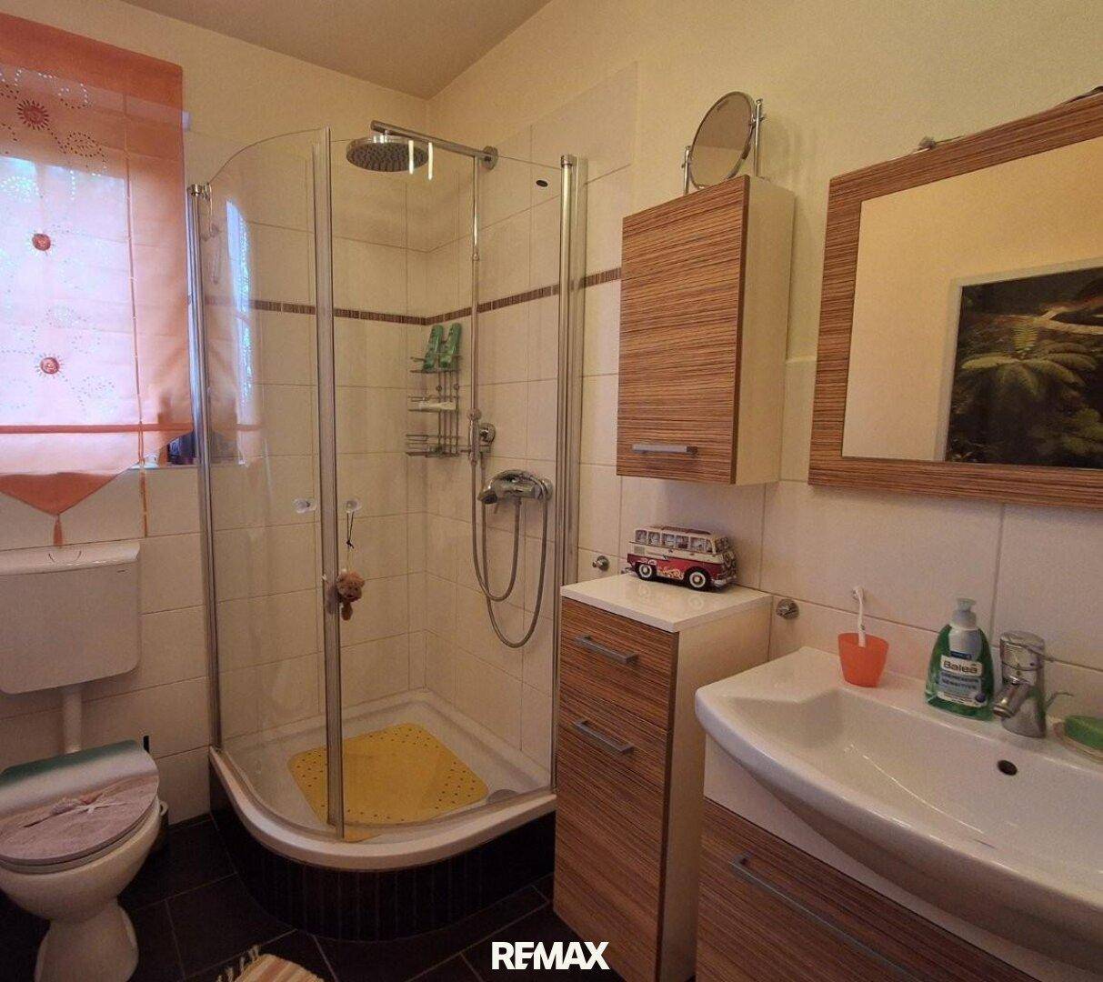 Badezimmer mit Eckdusche, Waschbecken und WC, ausgestattet mit hellen Fliesen.