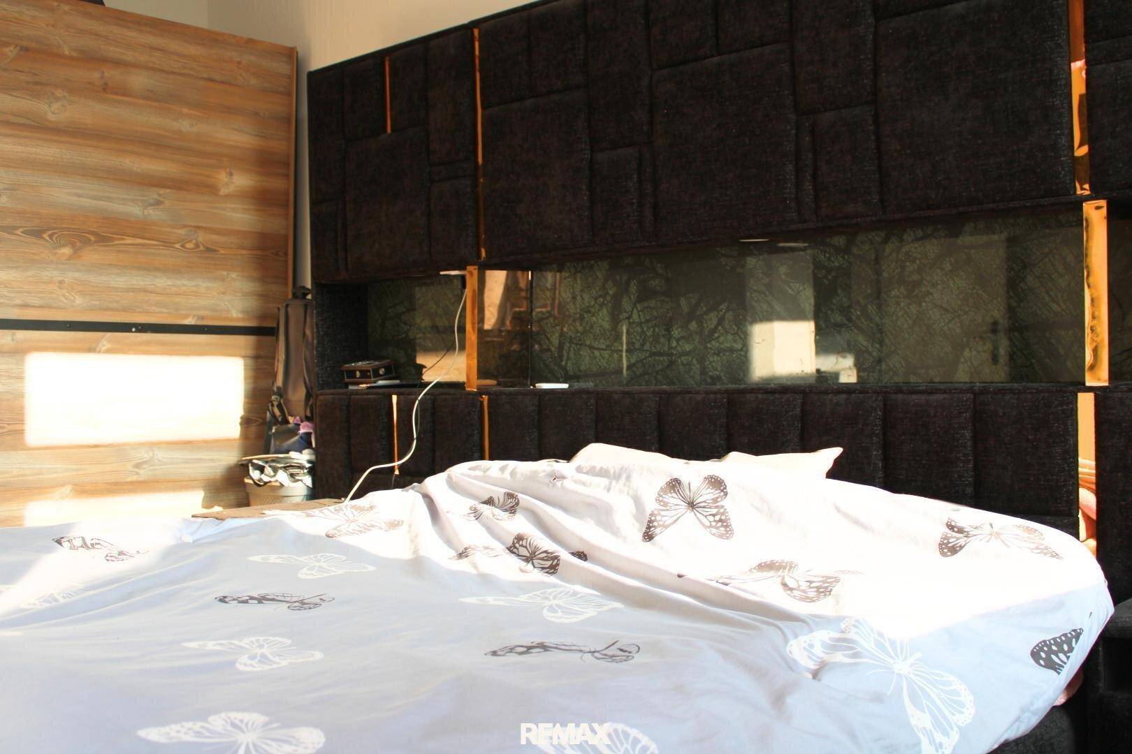 Schlafzimmer mit großem Bett, dunklem Kopfteil und Holzwandverkleidung.