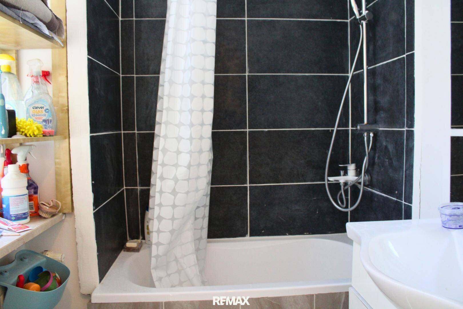 Badezimmer mit Badewanne, Duschvorhang und schwarzen Fliesen.
