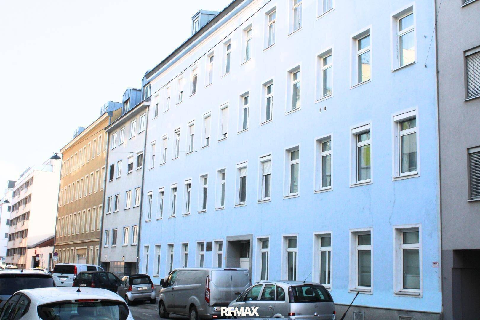 Mehrstöckiges Wohngebäude mit blauer Fassade und vielen Fenstern an einer Straße.