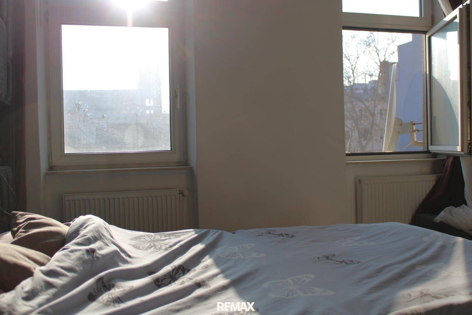 Helles Schlafzimmer mit zwei Fenstern, Heizkörpern und einem gemütlichen Bett.