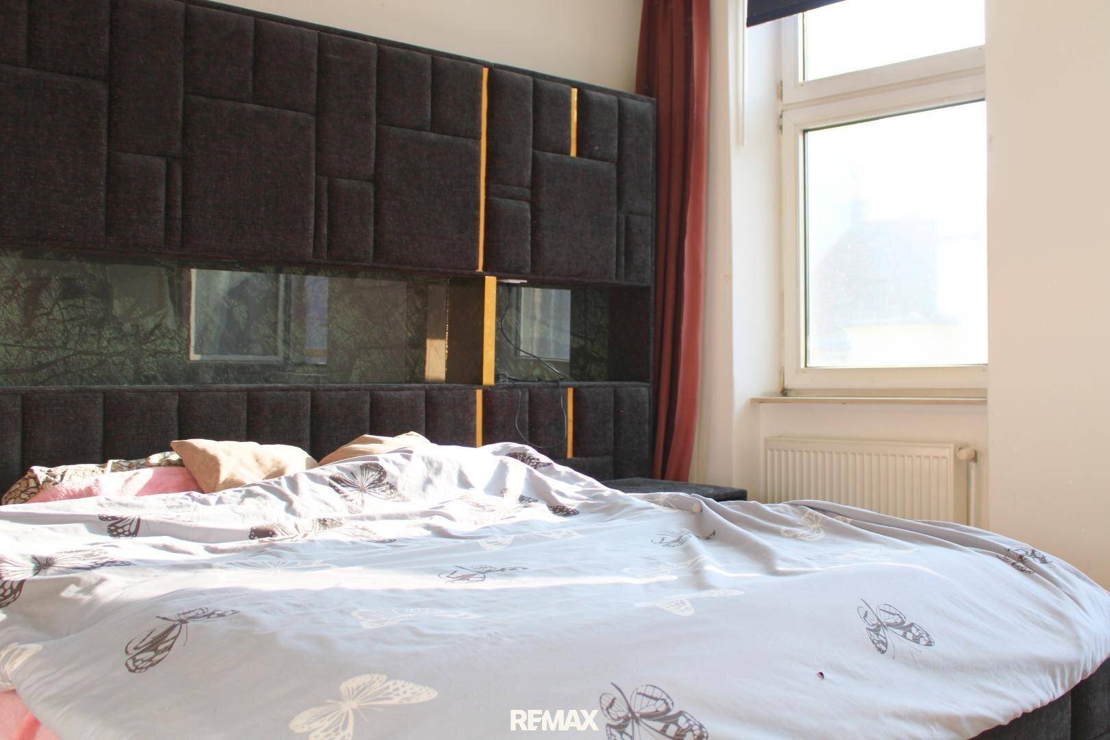 Schlafzimmer mit großem Bett, auffälligem Kopfteil und viel Tageslicht durch das Fenster.