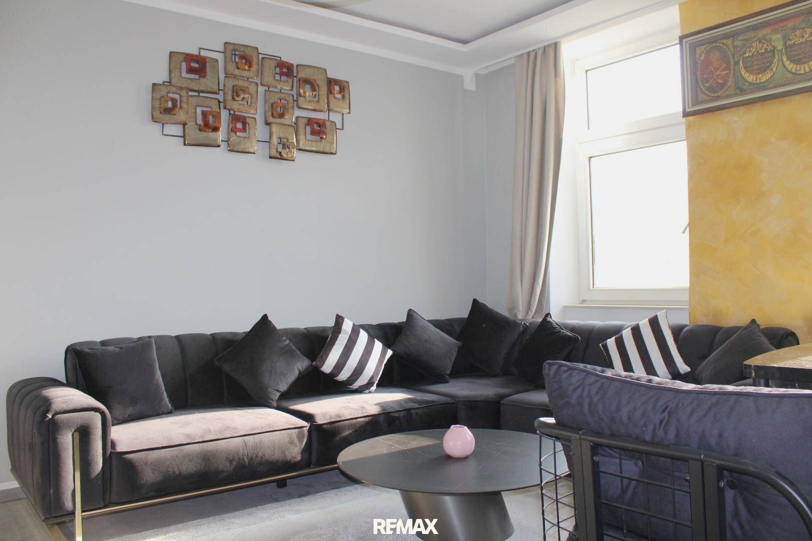 Geräumiges Wohnzimmer mit einem großen Ecksofa, modernen Wanddekorationen und viel Tageslicht.