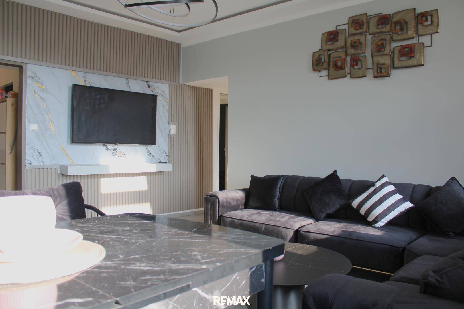Moderner Wohnbereich mit großem Fernseher an einer strukturierten Wand und dunklem Ecksofa.