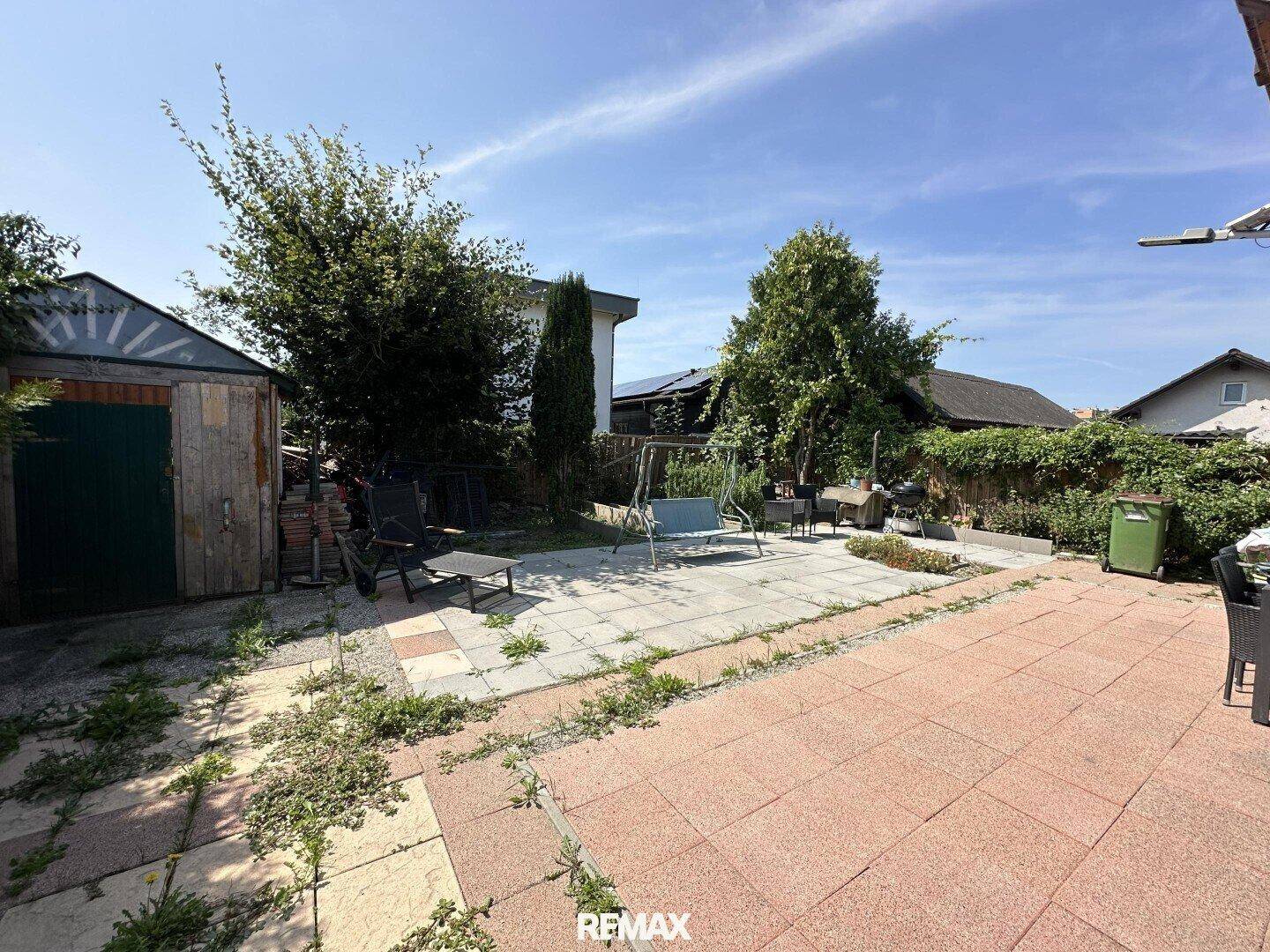 Großer Garten mit gepflastertem Bereich, Gartenhaus und viel Grünfläche.