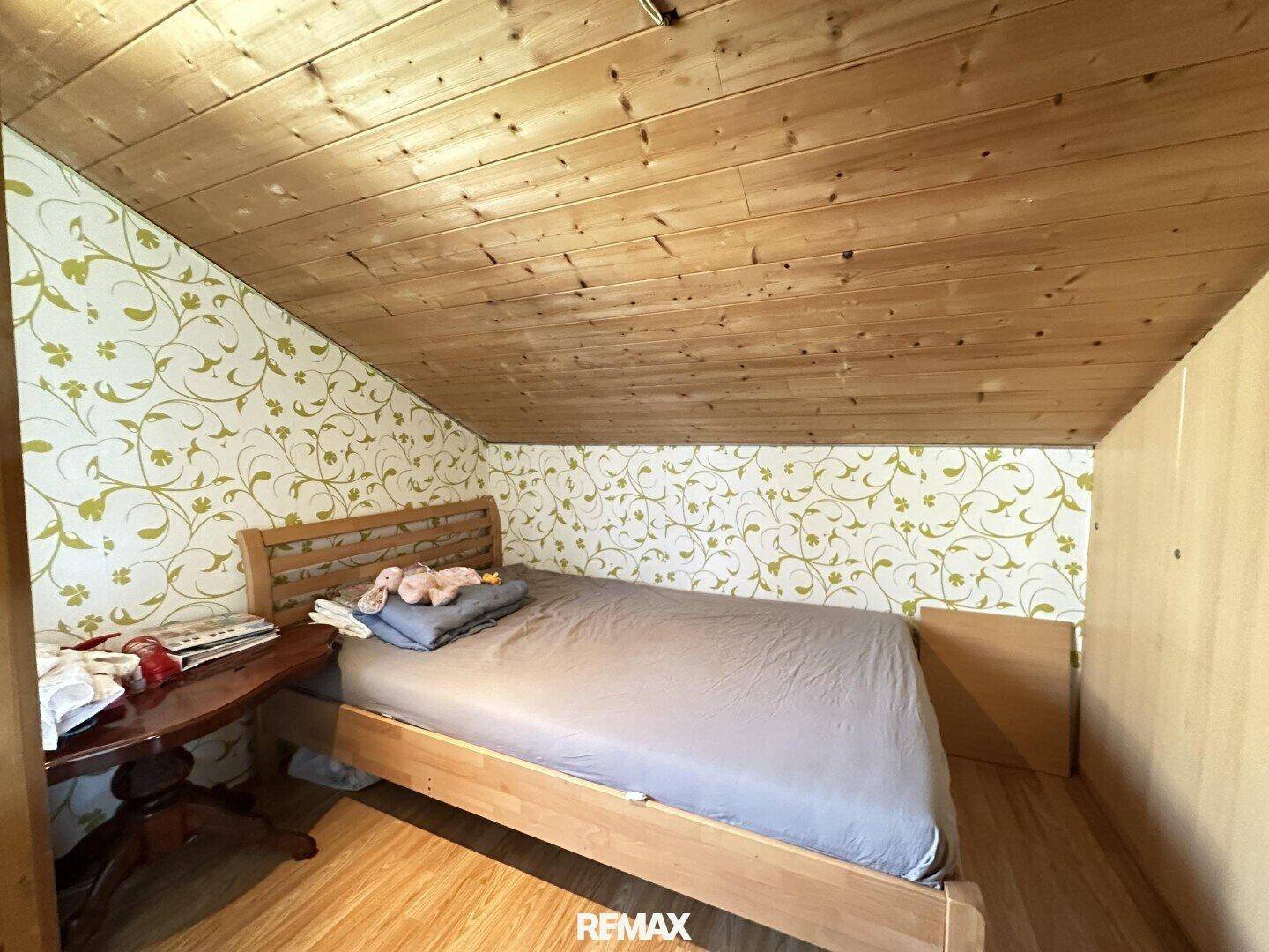 Schlafzimmer im Dachgeschoss mit floraler Tapete, Holztäfelung und Dachschräge.