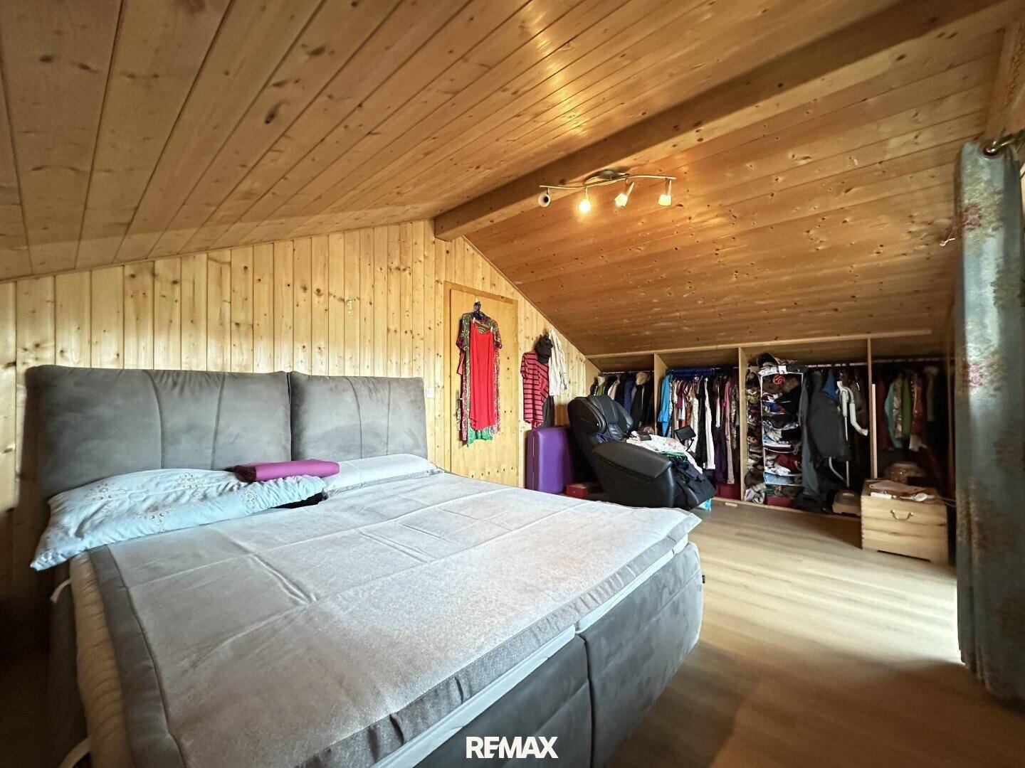 Schlafzimmer im Dachgeschoss mit Holztäfelung, Dachschräge und offenem Kleiderschrank.