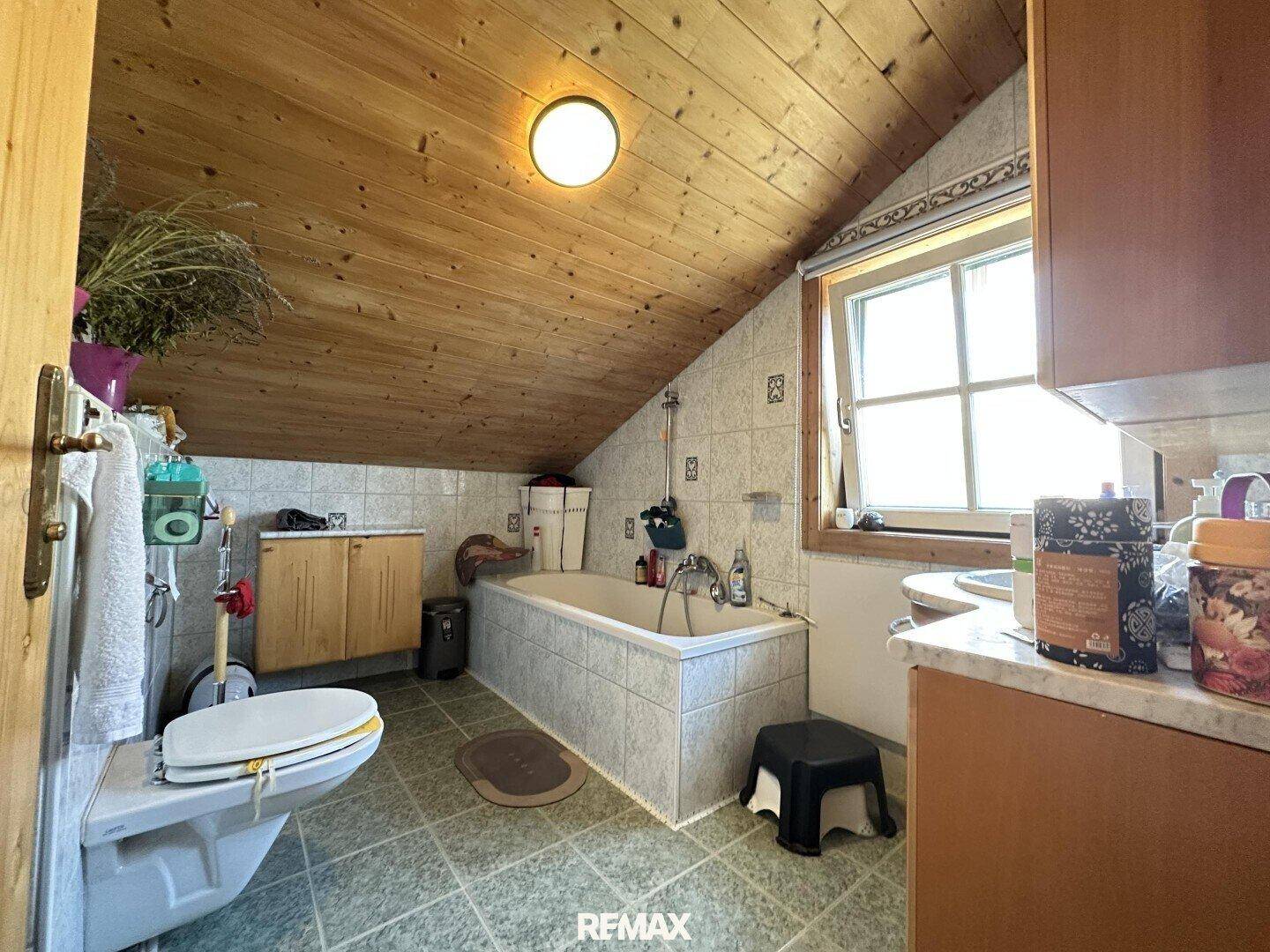 Badezimmer im Dachgeschoss mit Badewanne, WC, Fliesen und Holztäfelung.