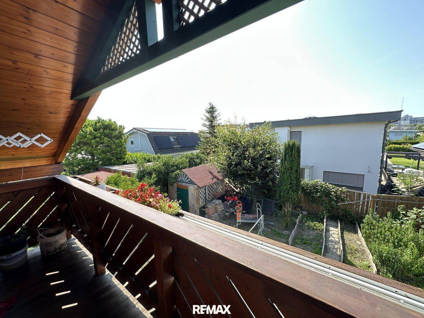 Balkon mit Holzgeländer und Blick auf den Garten sowie die umliegenden Häuser.