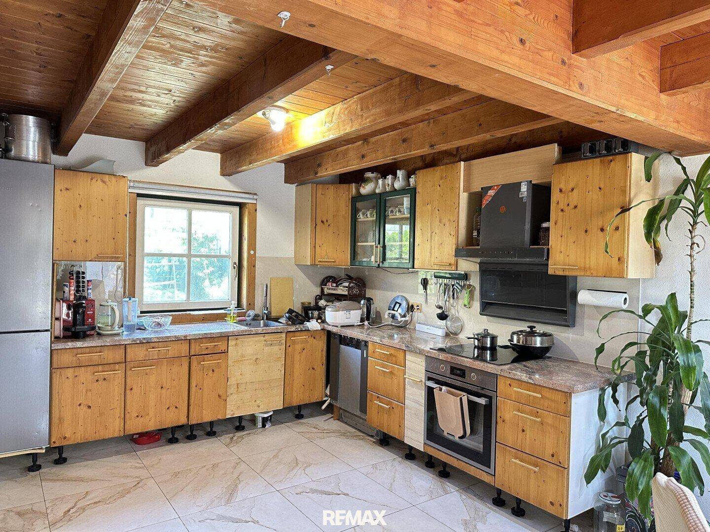 Rustikale Küche mit Holzschränken, Fliesenboden und Blick in den Garten.