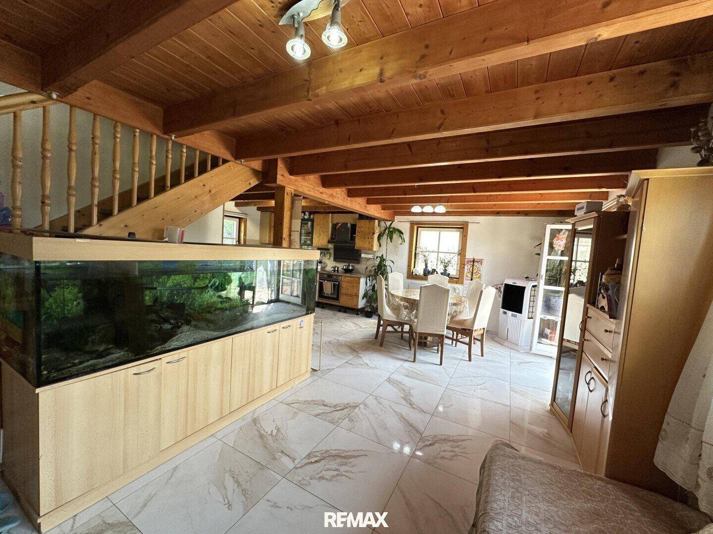 Geräumiger Wohn- und Essbereich mit großem Aquarium, Holztreppe und Fliesenboden.