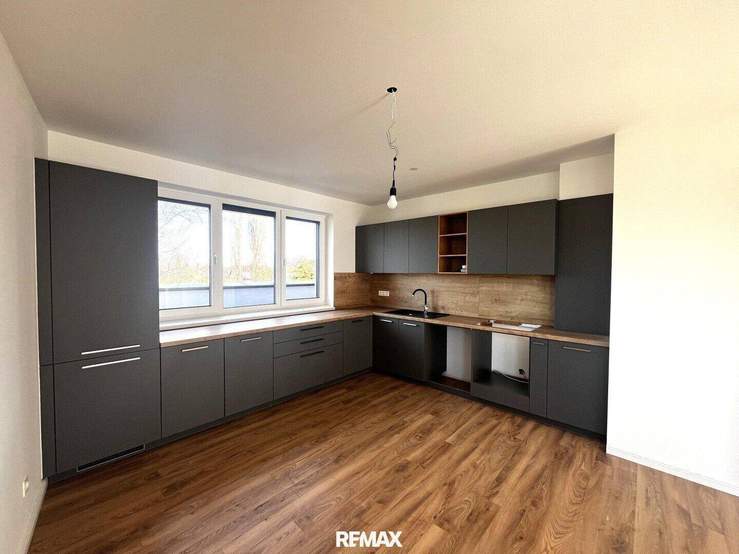 Moderne Küche mit grauen Schränken, Holzoptik-Arbeitsplatten und großem Fenster.