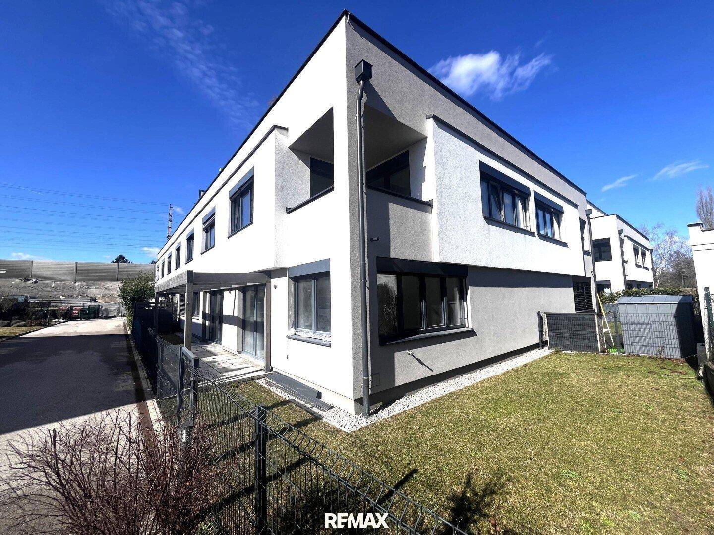 Seitenansicht eines modernen Gebäudes mit weißer und grauer Fassade, umgeben von Rasenflächen.