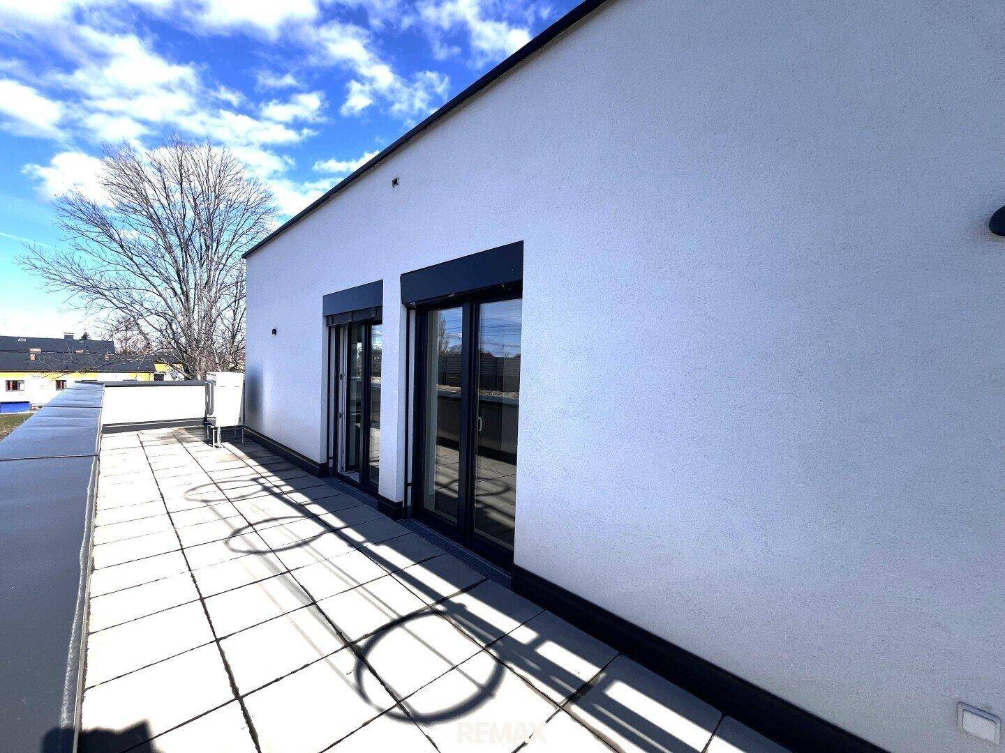 Sonniger Terrassenbereich mit Fliesenboden und Zugang zu den Wohnräumen, umgeben von einer modernen Fassade.