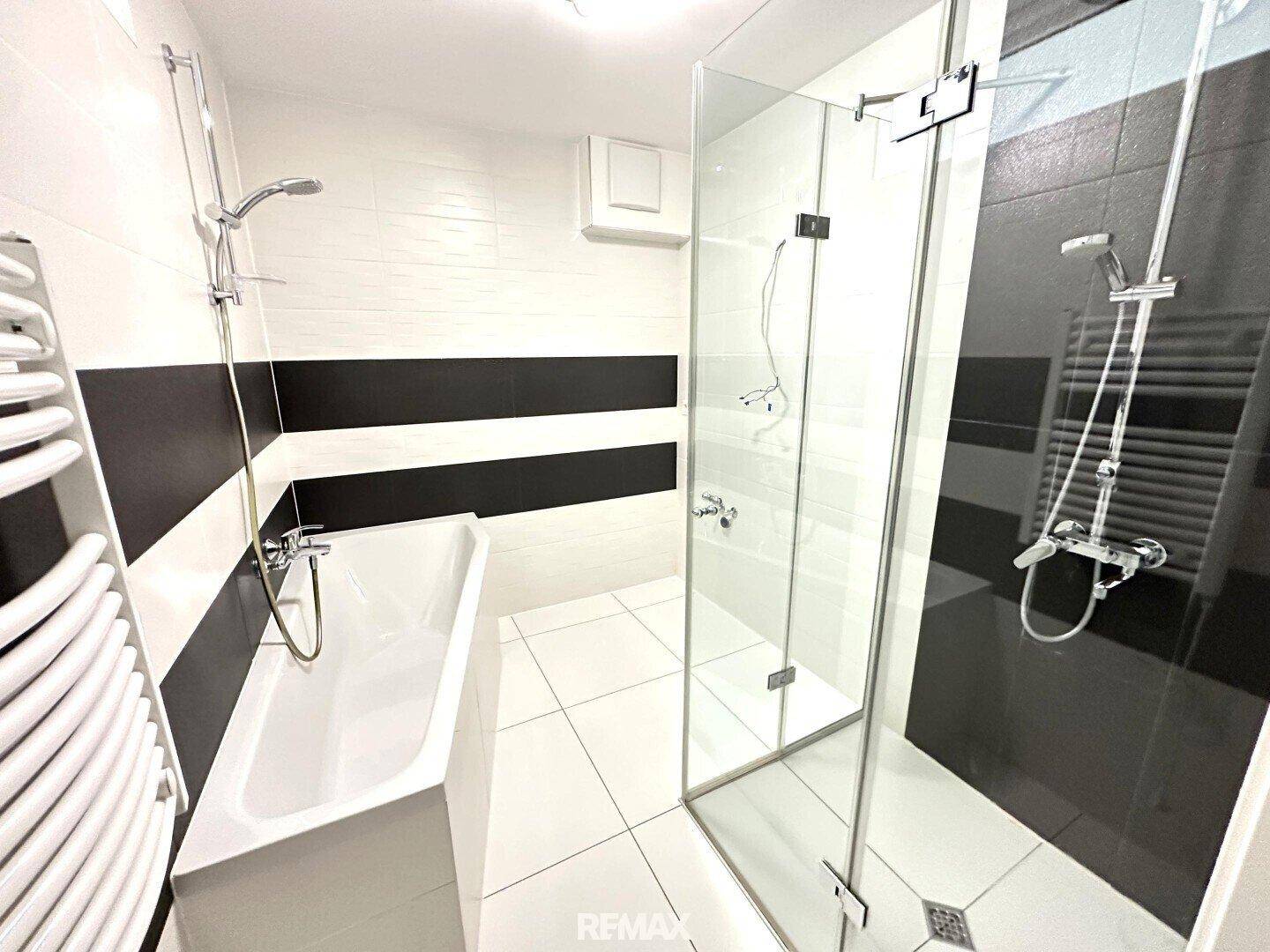 Modernes Badezimmer mit weißen und schwarzen Fliesen, Badewanne und begehbarer Dusche.