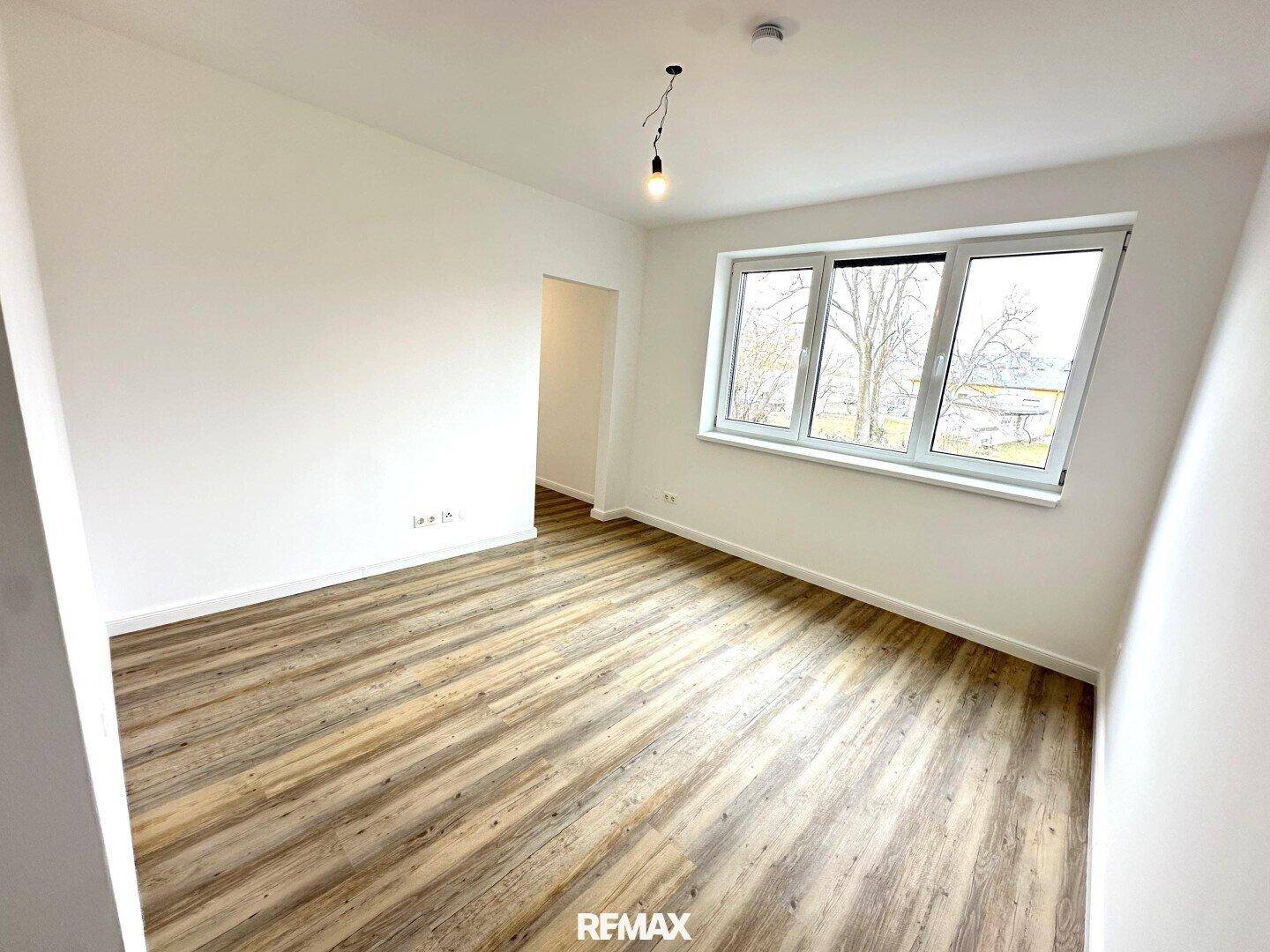 Geräumiges Schlafzimmer mit hellem Laminatboden und einem großen Fenster für natürliche Belichtung.