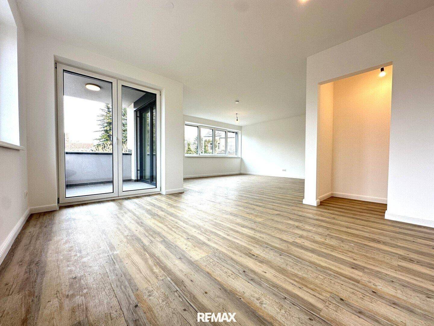 Geräumiger, heller Wohnbereich mit Laminatboden und großen Fenstern, die viel Licht hereinlassen.
