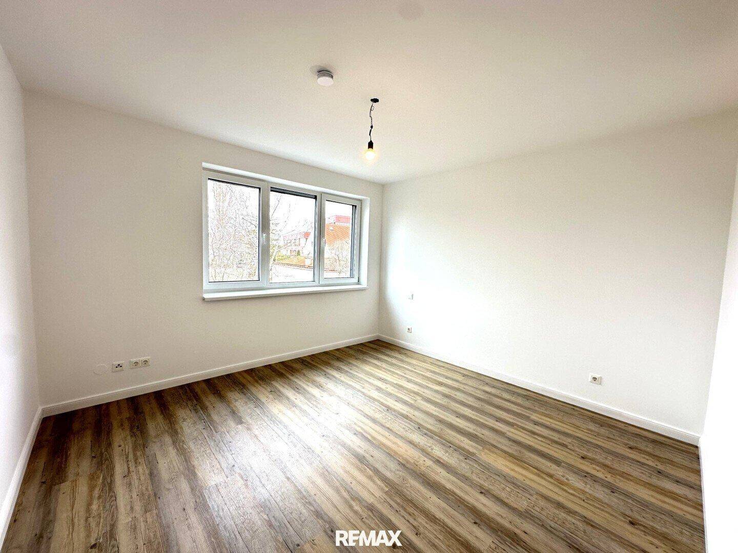 Helles Schlafzimmer mit Laminatboden und einem Fenster, das viel Tageslicht spendet.