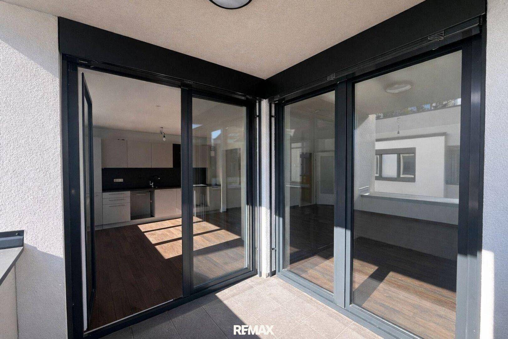 Blick vom Balkon in den Innenraum mit moderner Küche und dunklem Holzfußboden.