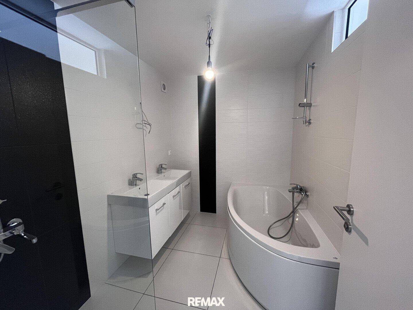Modernes Badezimmer mit weißen Fliesen, Doppelwaschbecken, Eckbadewanne und Duschbereich.