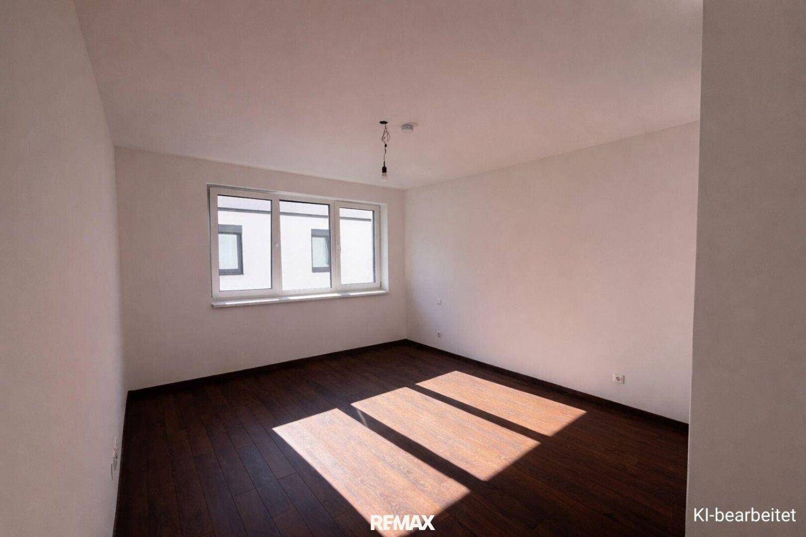 Helles, leeres Schlafzimmer mit dunklem Parkettboden und einem großen Fenster.