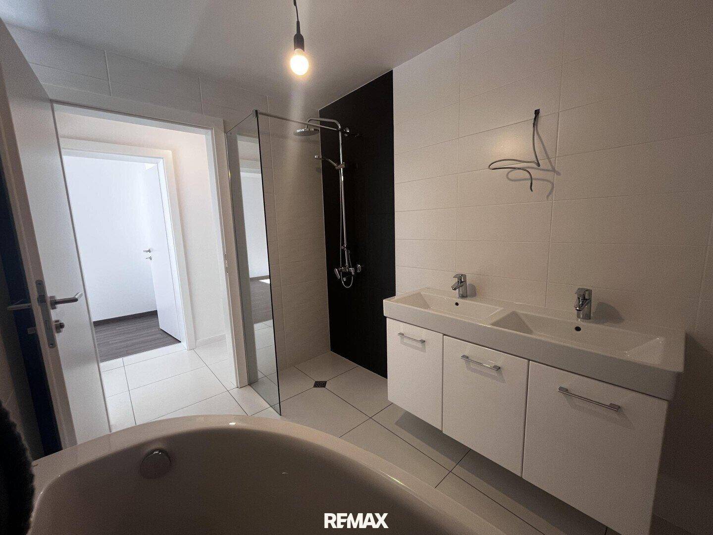 Modernes Badezimmer mit weißen Fliesen, Doppelwaschbecken, Duschbereich und Eckbadewanne.