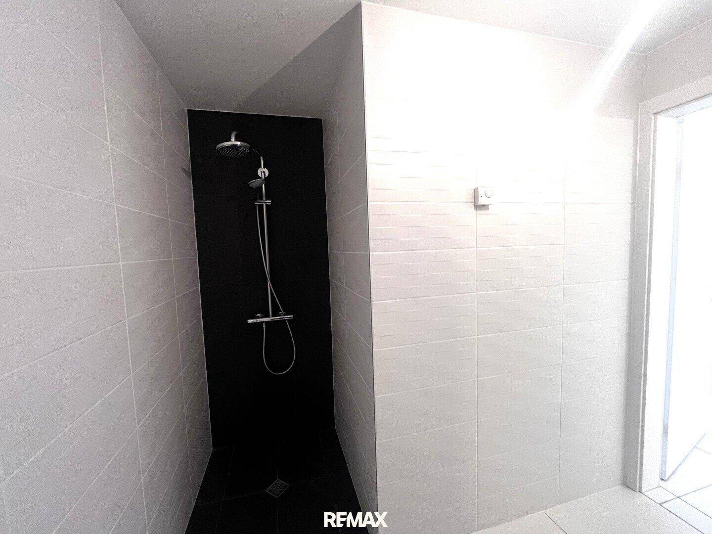 Geräumiger Duschbereich im Badezimmer mit eleganten schwarzen Fliesen an Wand und Boden.